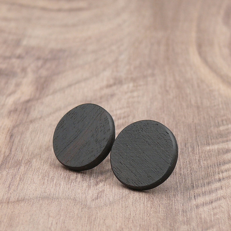 May include: Two black wooden circle earrings. The earrings are smooth and have a slightly textured surface.
