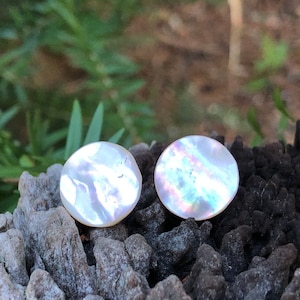 May include: A pair of iridescent white shell earrings. The earrings are round and have a smooth, polished finish.