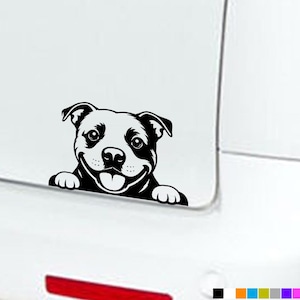 Könnte beinhalten: Ein schwarzer Vinyl-Aufkleber eines lächelnden Hundes, dessen Vorderpfoten auf einer Kante ruhen, angebracht auf einer weißen Oberfläche. Die Grafik zeigt kontrastreiche schwarze Linien, die das Gesicht, die Ohren und die Pfoten des Hundes darstellen.