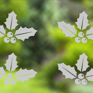 Op de afbeelding: Vier witte designs met hulstbladeren en bessen op een groene achtergrond.