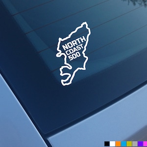 May include: White vinyl sticker of a map of the North Coast 500 route in Scotland. The sticker is on a blue car window.