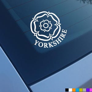 May include: A white vinyl decal applied to a dark car window, featuring a stylized heraldic rose emblem centered above the text YORKSHIRE in a bold, serif font. The design is clean, monochromatic, and adheres directly to the glass surface.