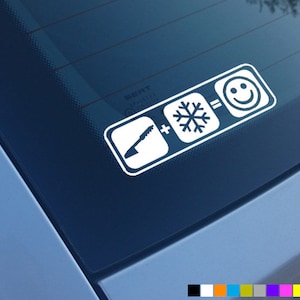 Pode incluir: Adesivo de vinil branco com um gráfico de uma pá, um sinal de mais, um floco de neve, um sinal de igual e um rosto sorridente. O adesivo está em uma janela de carro azul.