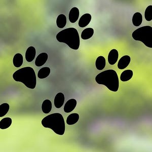 May include: Black paw print decals arranged in a pattern against a blurred green and white background. The paw prints are a simple, solid design, suitable for pet-themed crafts or decor.