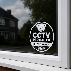 Pode incluir: Um autocolante circular para janela em branco e preto com um gráfico de uma câmara de segurança, o texto "CCTV PROTECTED" e "SILENT ALARM", e um pequeno ícone de cadeado com ondas de sinal, aplicado numa superfície de vidro.