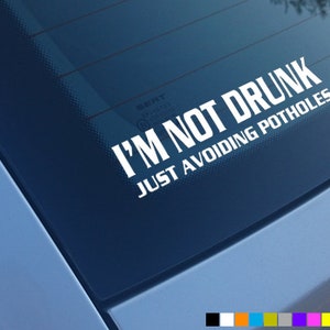 Może przedstawiać: Biała naklejka winylowa z tekstem "Nie jestem pijany, po prostu unikam dziur" na niebieskim oknie samochodu.