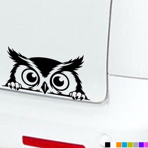 Pode incluir: Um autocolante de vinil preto com uma coruja estilizada com olhos grandes e redondos e orelhas com tufos, representada como se estivesse a espreitar por cima de uma borda. O design inclui duas pequenas garras visíveis na parte inferior.