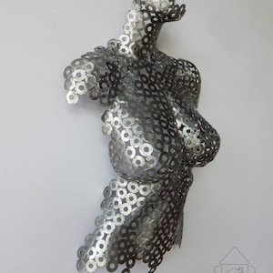 May include: A silver metal sculpture of a torso made from hundreds of small metal washers. The sculpture is abstract and has a modern design.