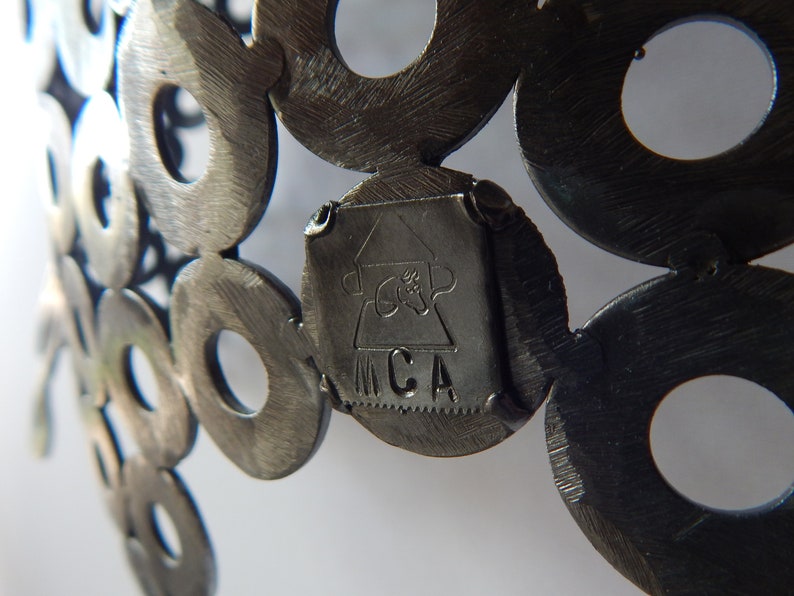 May include: Close-up of a metal sculpture made of interlocking circles. The sculpture has a small, rectangular tag attached to it with the letters "MCA" inscribed on it.