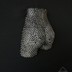 May include: A three-dimensional sculpture of a human form made entirely of silver metal nuts. The sculpture is a stylized representation of a human body, with the nuts arranged in a pattern that creates the illusion of curves and contours.
