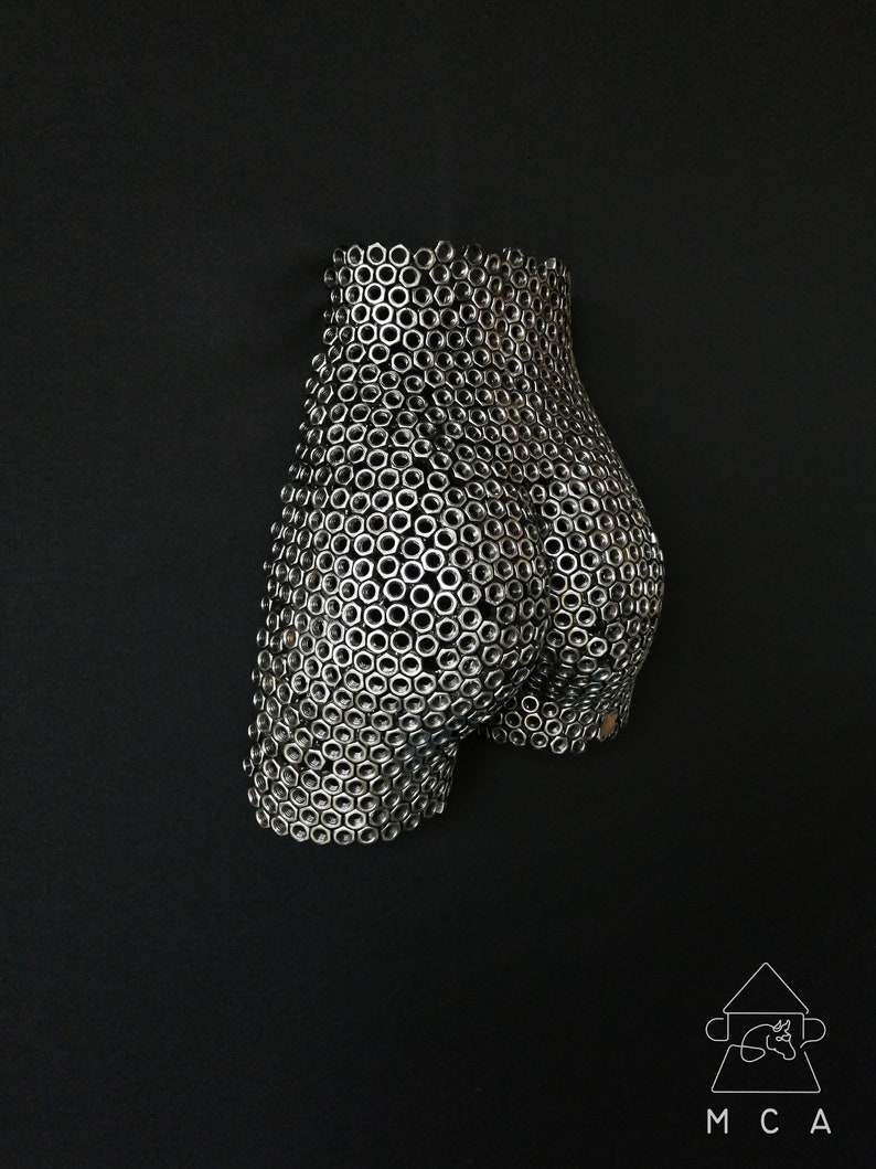 May include: A three-dimensional sculpture of a human form made entirely of silver metal nuts. The sculpture is a stylized representation of a human body, with the nuts arranged in a pattern that creates the illusion of curves and contours.