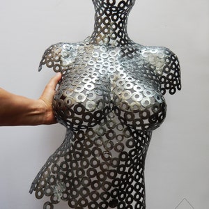 May include: A silver metal sculpture of a torso made from a series of interlocking metal washers.