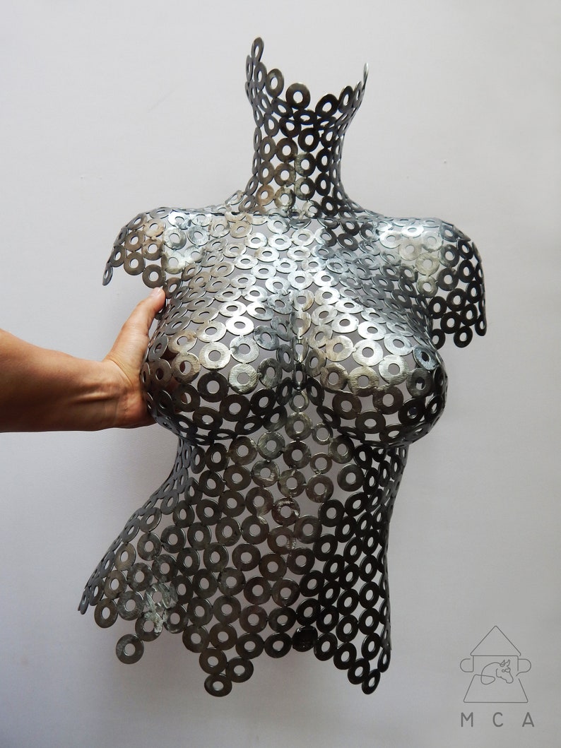 May include: A silver metal sculpture of a torso made from a series of interlocking metal washers.