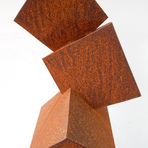 K&ouml;nnte beinhalten: Abstrakte Skulptur aus gestapelten, verwitterten, quadratischen Metallbl&ouml;cken. Die rostig-orangebraune Farbe und die geometrischen Formen erzeugen eine moderne, industrielle &Auml;sthetik. Das Design der Skulptur zeigt eine dynamische, ausgewogene Anordnung.