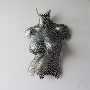 May include: A silver metal sculpture of a torso made from a pattern of interlocking metal washers.