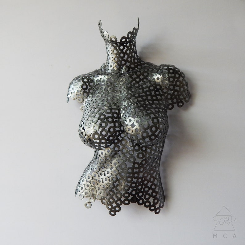 May include: A silver metal sculpture of a torso made from a pattern of interlocking metal washers.