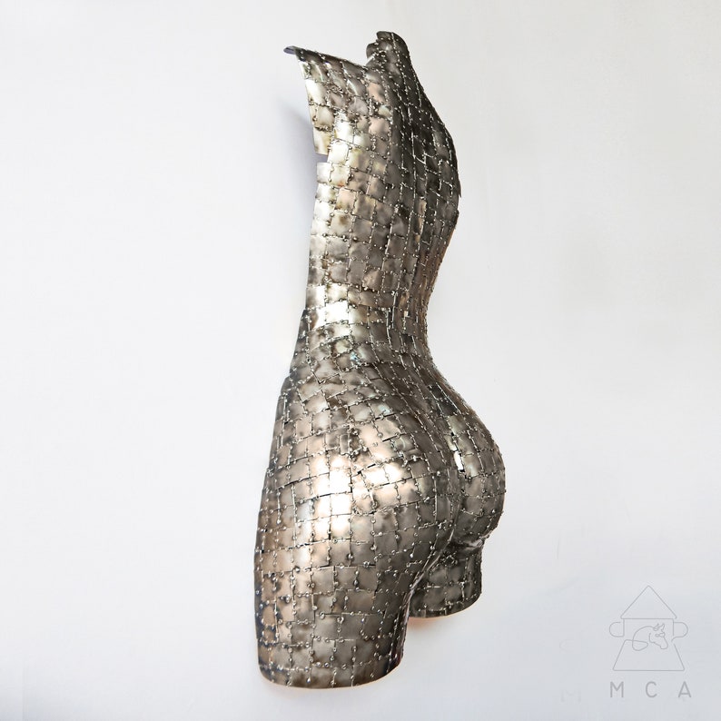 This photograph shows a metal sculpture with a female figure, made with hundreds of pieces of metal sheet that each do not exceed one inch in size, welded one by one until forming the beautiful hips of a woman and part of your back