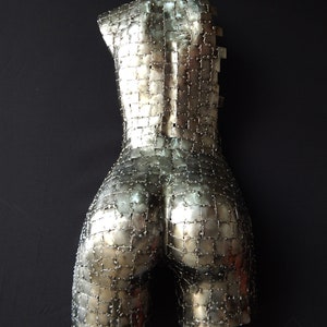 This photograph shows a metal sculpture with a female figure, made with hundreds of pieces of metal sheet that each do not exceed one inch in size, welded one by one until forming the beautiful hips of a woman and part of your back