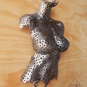 May include: A silver and black metal sculpture of a torso made from washers. The sculpture is mounted on a wooden wall.