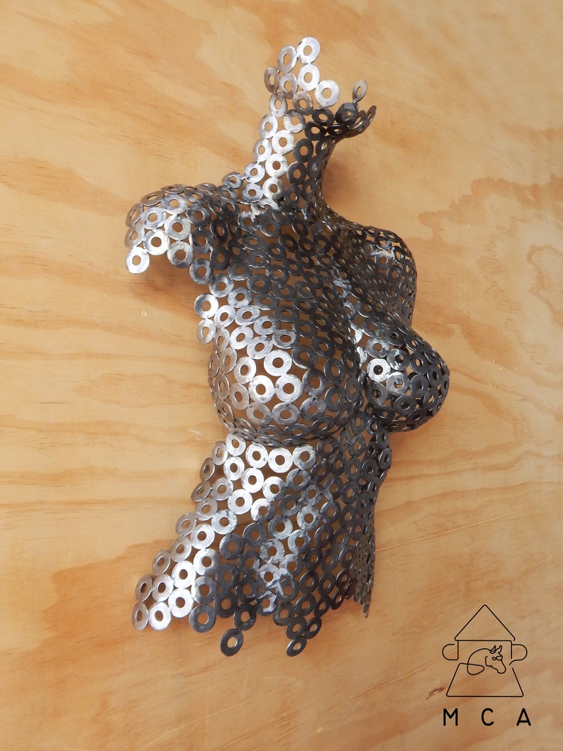 May include: A silver and black metal sculpture of a torso made from washers. The sculpture is mounted on a wooden wall.
