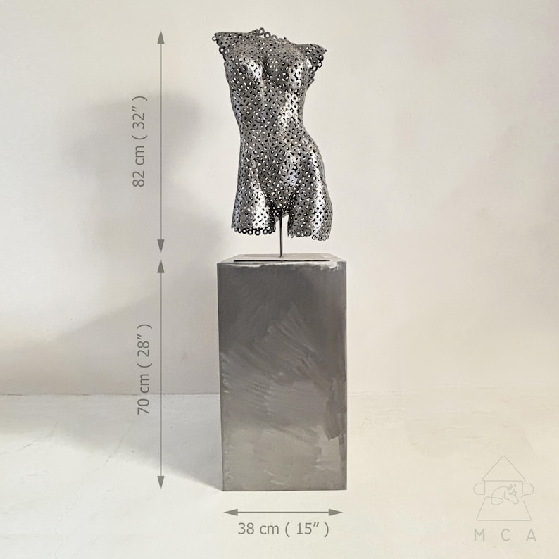 May include: A metal sculpture of a torso, 32 inches tall, with a perforated design, mounted on a 28-inch tall rectangular pedestal. The pedestal is 15 inches wide. The sculpture is a modern art piece.