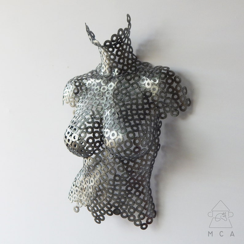 May include: A silver metal sculpture of a torso made from hundreds of small metal washers. The sculpture is a modern art piece.