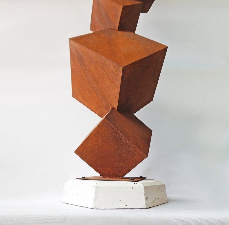 K&ouml;nnte beinhalten: Abstrakte Skulptur mit gestapelten, geometrischen W&uuml;rfeln in Rostbraun. Die W&uuml;rfel sind auf einem wei&szlig;en, geometrischen Sockel montiert. Das Kunstwerk hat eine moderne, industrielle &Auml;sthetik.