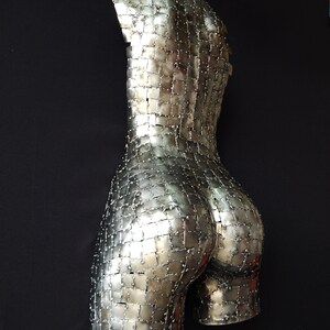 This photograph shows a metal sculpture with a female figure, made with hundreds of pieces of metal sheet that each do not exceed one inch in size, welded one by one until forming the beautiful hips of a woman and part of your back