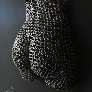 May include: A wall sculpture made of metal nuts, shaped like a human body. The sculpture is black and has a textured surface.