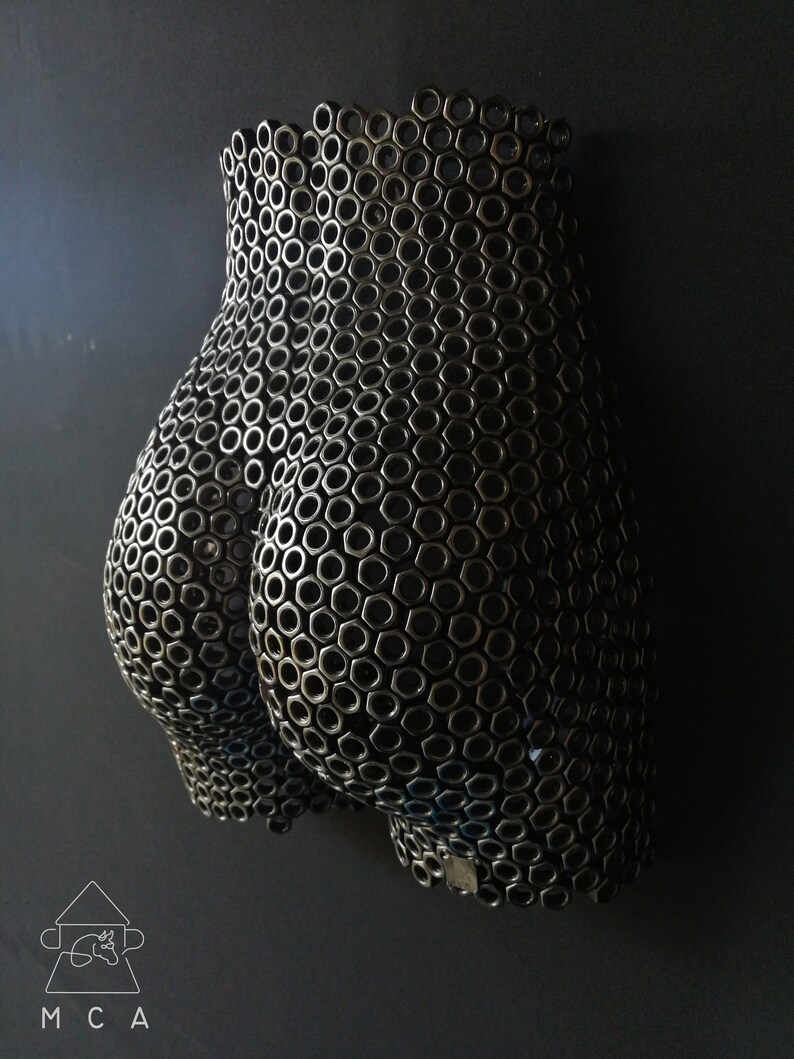 May include: A wall sculpture made of metal nuts, shaped like a human body. The sculpture is black and has a textured surface.
