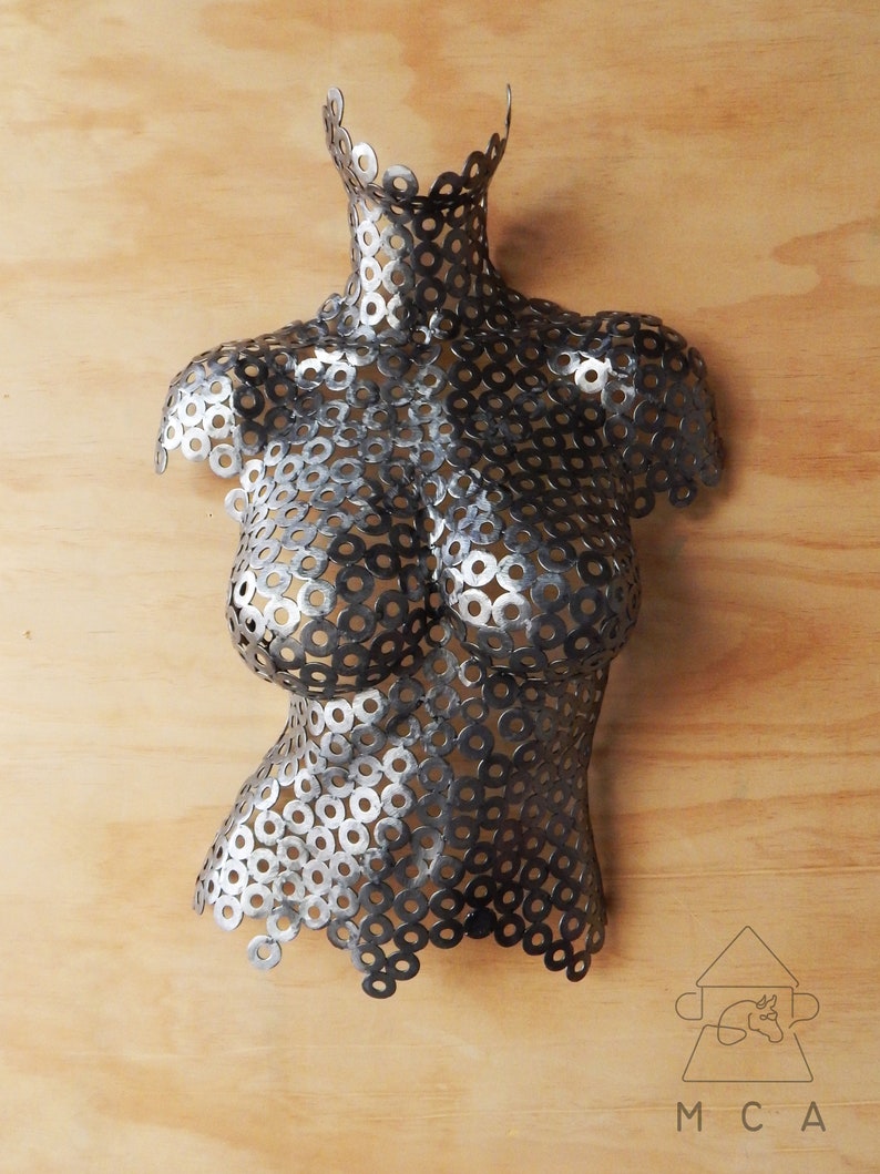 May include: A silver metal sculpture of a torso made from many small metal rings. The sculpture is mounted on a wooden surface.