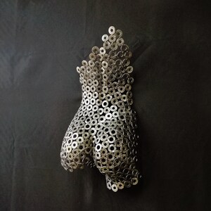 May include: A silver metal sculpture of a human torso made from many small metal washers.