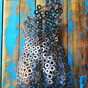 May include: A metal sculpture of a human torso made from a collection of silver metal washers. The sculpture is mounted on a blue and brown wooden background.
