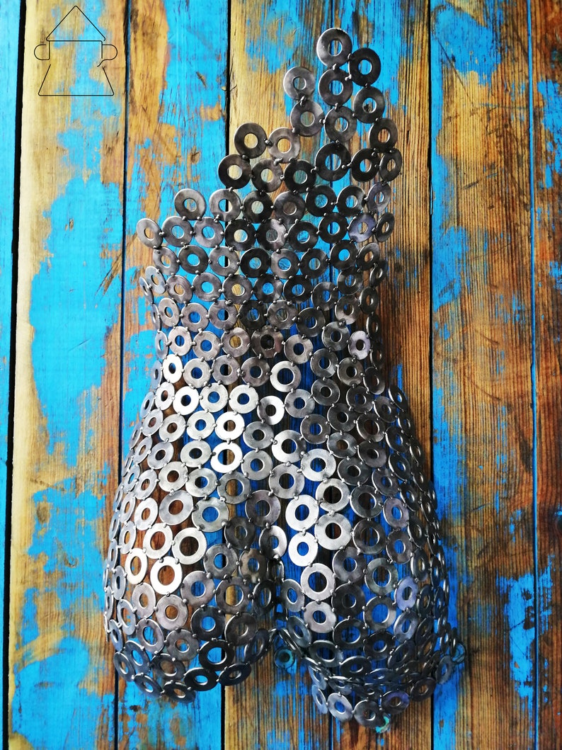 May include: A metal sculpture of a human torso made from a collection of silver metal washers. The sculpture is mounted on a blue and brown wooden background.