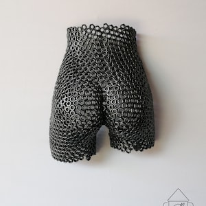 May include: A black metal sculpture of a human body, made from a grid of interlocking metal rings.