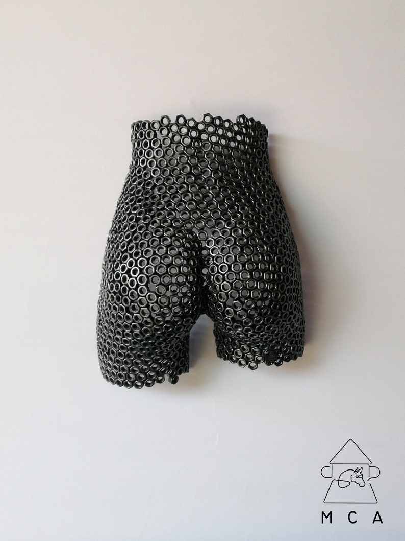 May include: A black metal sculpture of a human body, made from a grid of interlocking metal rings.