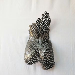 May include: A metal sculpture of a human torso made from hundreds of small, silver-colored metal rings.