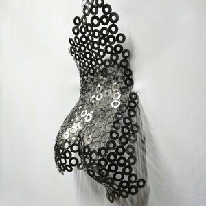 May include: A silver metal sculpture of a torso made from a series of interlocking metal rings.