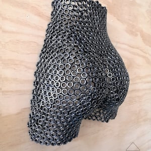 May include: A wall sculpture made of metal nuts, shaped like a human body. The sculpture is painted in a dark gray color.
