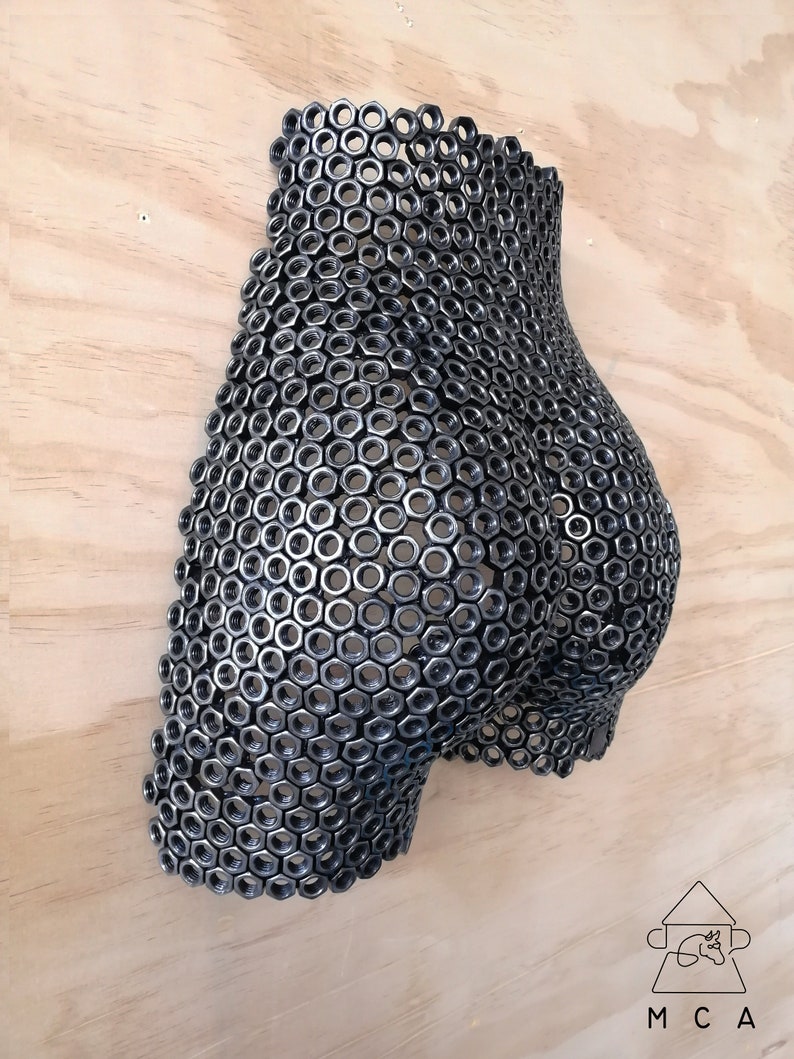 May include: A wall sculpture made of metal nuts, shaped like a human body. The sculpture is painted in a dark gray color.