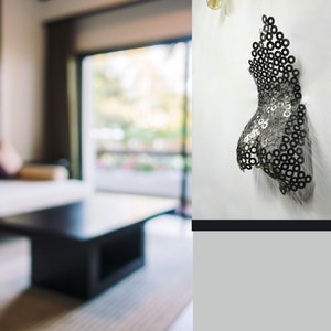 May include: A metal sculpture of a torso made of small metal rings. The sculpture is mounted on a white wall.