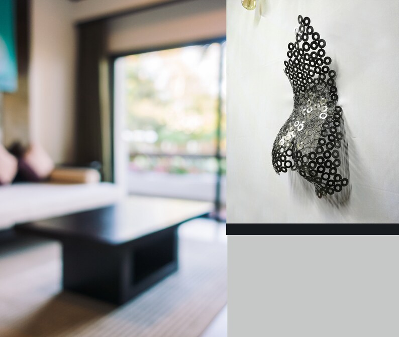 May include: A metal sculpture of a torso made of small metal rings. The sculpture is mounted on a white wall.