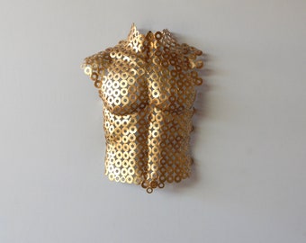 Può includere: Una scultura in metallo dorato di un torso realizzata con un motivo di cerchi intrecciati.
