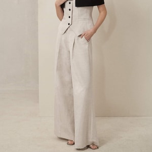 May include: A woman wearing a black cropped blazer over a light gray vest and matching wide-leg pants. She is wearing gold hoop earrings and a silver chain necklace.