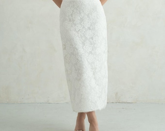 May include: A two-piece white lace ensemble consisting of a sleeveless camisole top with thin spaghetti straps and a scalloped neckline, paired with a high-waisted, floor-length skirt featuring an intricate floral lace overlay pattern.