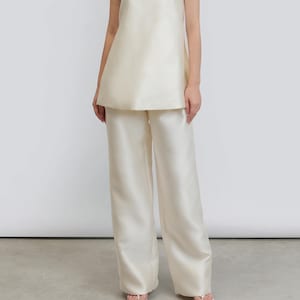 May include: Cream-coloured strapless top and wide-leg trousers ensemble. The top features a straight neckline and a gently flared silhouette. The trousers are high-waisted and flowing. The outfit is crafted from a smooth, silky fabric, ideal for special events.