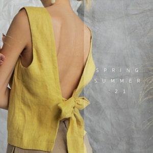 May include: A yellow linen top with a low back and a bow tie detail. The top is sleeveless and has a relaxed fit. The text "SPRING SUMMER '21" is visible in the background.