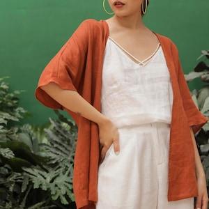 May include: A rust-colored linen kimono with 3/4 sleeves worn over a white linen tank top and white linen pants.