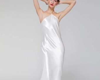 May include: A white halter-style maxi dress made of silky fabric. The dress has a simple design and a flowing silhouette.