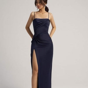 May include: A navy blue, floor-length, sleeveless dress with a side slit and a knot detail at the waist.